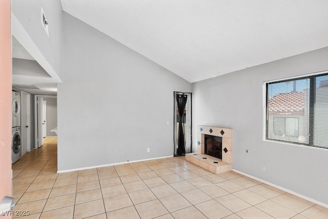 unfurnished living room with light tile patterned floors, baseboards, a tile fireplace, and stacked washer / drying machine