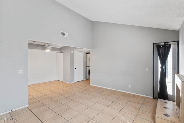 empty room with light tile patterned floors, visible vents, baseboards, stacked washer and clothes dryer, and ceiling fan