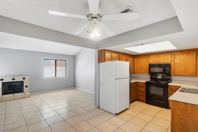 kitchen with brown cabinets, light countertops, black appliances, a fireplace, and light tile patterned flooring