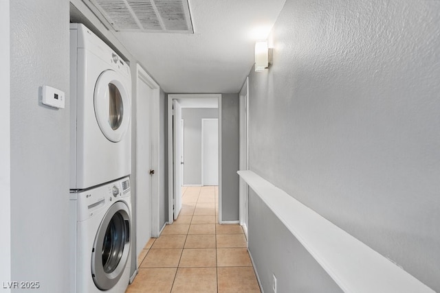 laundry room featuring laundry area, visible vents, stacked washing maching and dryer, and light tile patterned floors