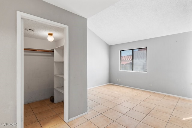 unfurnished bedroom with lofted ceiling, a closet, a textured ceiling, baseboards, and tile patterned floors