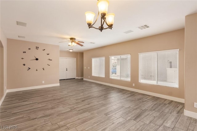 empty room featuring light wood finished floors, baseboards, visible vents, and ceiling fan with notable chandelier