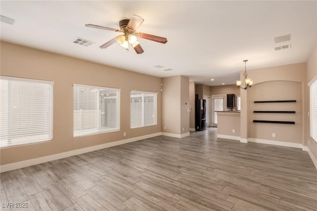 unfurnished living room with dark wood-style flooring, visible vents, baseboards, and ceiling fan with notable chandelier