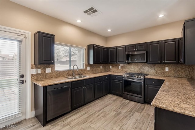 kitchen with visible vents, light wood-style flooring, a sink, stainless steel appliances, and backsplash