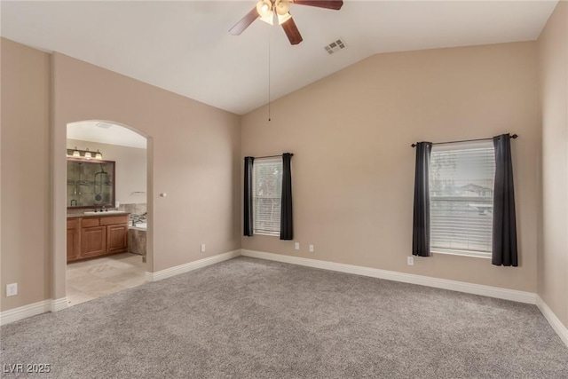 unfurnished bedroom featuring arched walkways, lofted ceiling, light colored carpet, visible vents, and ensuite bath