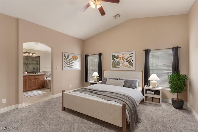 bedroom with arched walkways, lofted ceiling, light colored carpet, visible vents, and ensuite bathroom