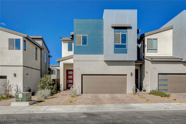 contemporary house with a garage, decorative driveway, cooling unit, and stucco siding