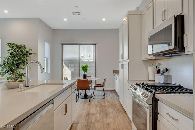 kitchen with light wood-style flooring, stainless steel appliances, a sink, visible vents, and light countertops