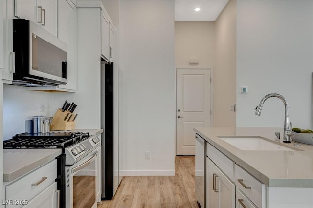 kitchen with light wood-style flooring, a sink, white cabinets, light countertops, and appliances with stainless steel finishes