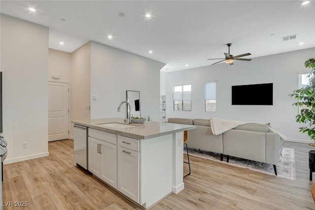 kitchen featuring light wood finished floors, stainless steel dishwasher, open floor plan, white cabinetry, and a sink