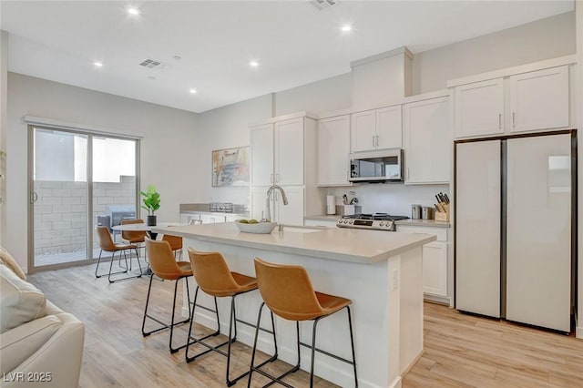 kitchen with a breakfast bar, light countertops, appliances with stainless steel finishes, a sink, and an island with sink