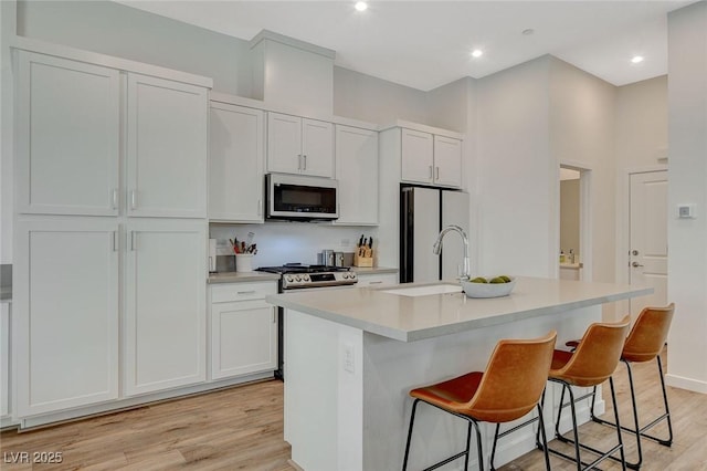 kitchen featuring a kitchen island with sink, stainless steel appliances, a sink, light countertops, and light wood-type flooring