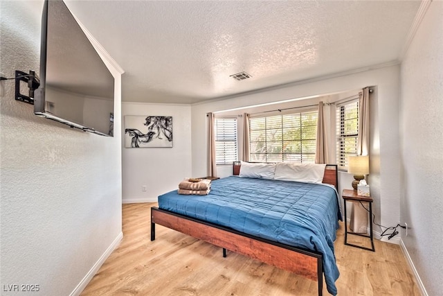 bedroom with visible vents, ornamental molding, a textured ceiling, and wood finished floors