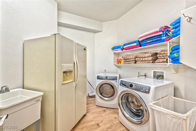 clothes washing area featuring laundry area, washing machine and dryer, light wood-style floors, and a sink