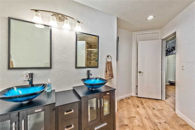 bathroom featuring a textured ceiling, wood finished floors, a textured wall, and a sink