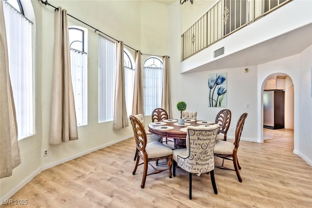 dining space featuring arched walkways, visible vents, light wood-type flooring, and baseboards