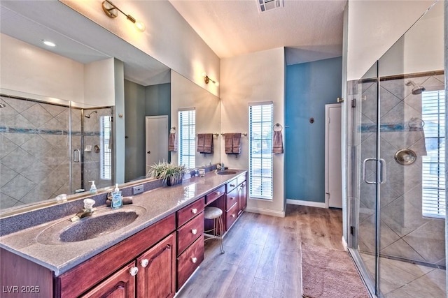 full bath featuring double vanity, wood finished floors, a shower stall, and a sink