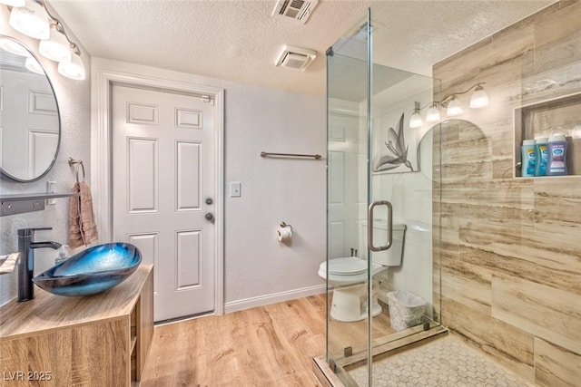 full bathroom with visible vents, toilet, a stall shower, wood finished floors, and a textured ceiling