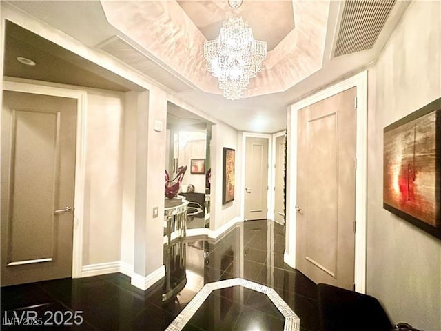 hall featuring a chandelier, a raised ceiling, visible vents, and baseboards