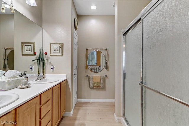 bathroom with wood finished floors, a sink, baseboards, double vanity, and a stall shower