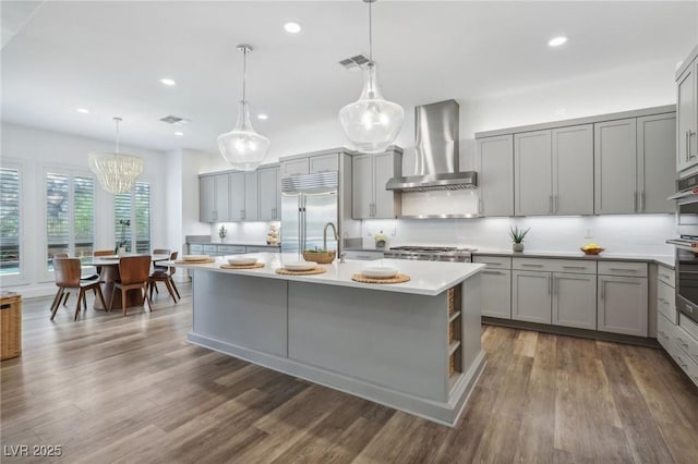 kitchen with appliances with stainless steel finishes, gray cabinets, wall chimney range hood, and tasteful backsplash