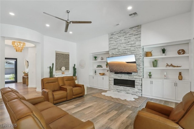 living area with a stone fireplace, light wood-type flooring, visible vents, and built in features