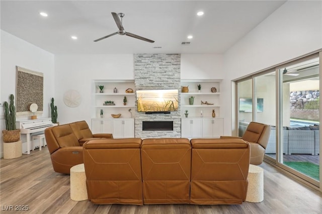 living area with light wood-style flooring, ceiling fan, built in shelves, a fireplace, and recessed lighting