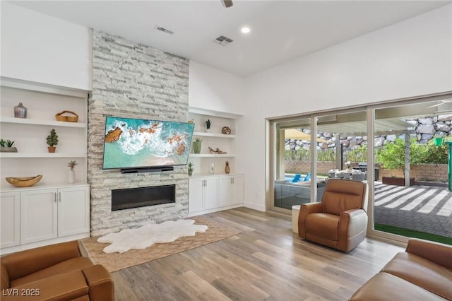 living room featuring light wood finished floors, built in shelves, visible vents, and a stone fireplace