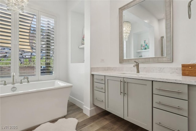 bathroom with a freestanding tub, wood finished floors, vanity, and baseboards