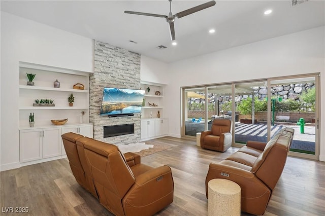 living room featuring built in shelves, recessed lighting, a fireplace, a ceiling fan, and light wood finished floors