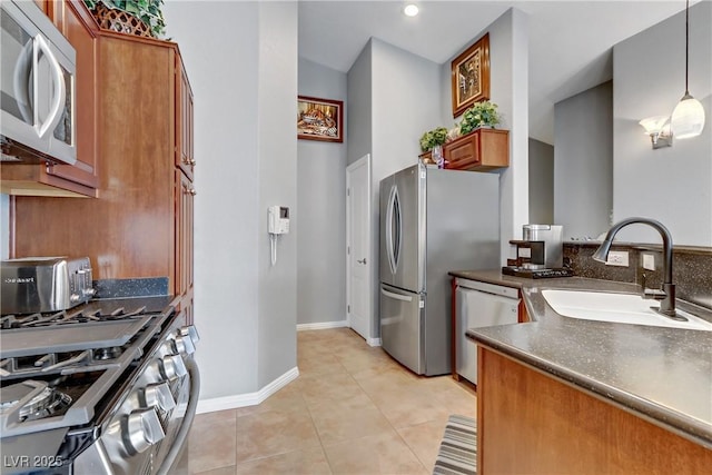 kitchen with light tile patterned floors, a sink, appliances with stainless steel finishes, brown cabinetry, and dark countertops