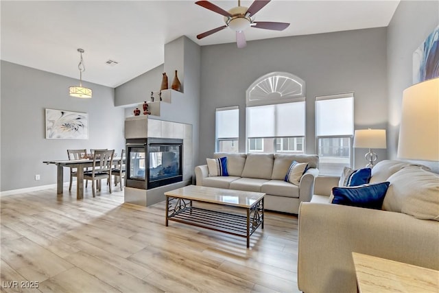 living area with high vaulted ceiling, a fireplace, visible vents, baseboards, and light wood-type flooring