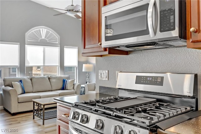 kitchen with brown cabinetry, a ceiling fan, light wood-style flooring, open floor plan, and stainless steel appliances