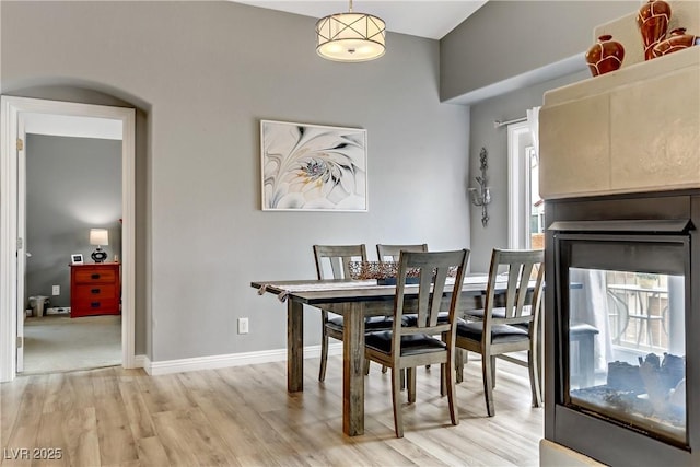 dining area with light wood-style floors, a multi sided fireplace, and baseboards