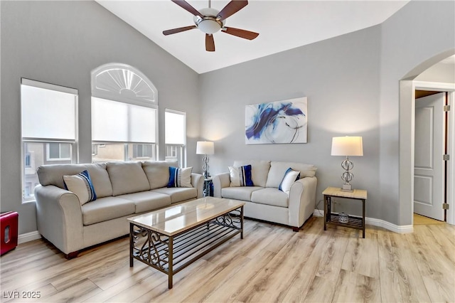 living area featuring light wood-style floors, baseboards, arched walkways, and vaulted ceiling