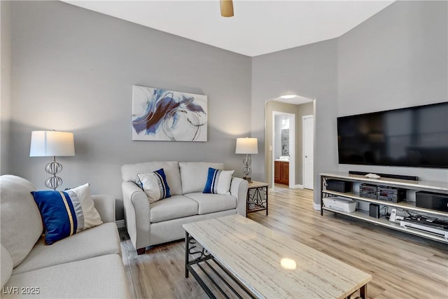 living area with baseboards, arched walkways, ceiling fan, and wood finished floors