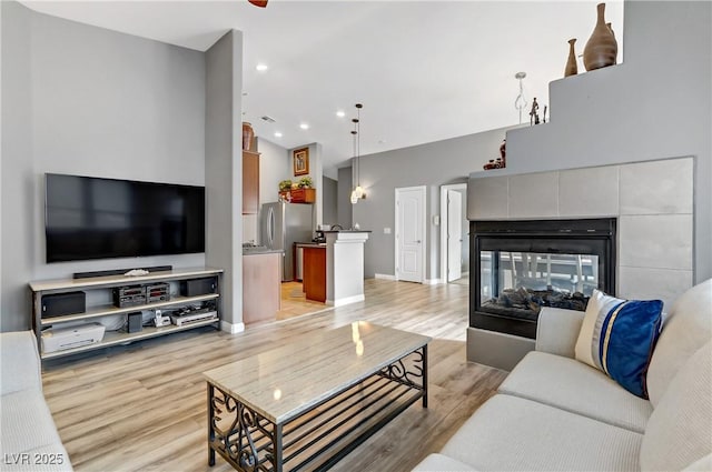 living room with light wood finished floors, baseboards, a tiled fireplace, and recessed lighting