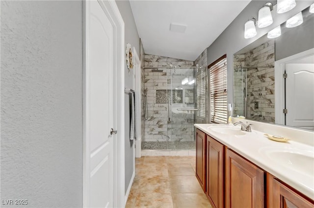 bathroom with a textured wall, tile patterned flooring, a sink, double vanity, and a stall shower