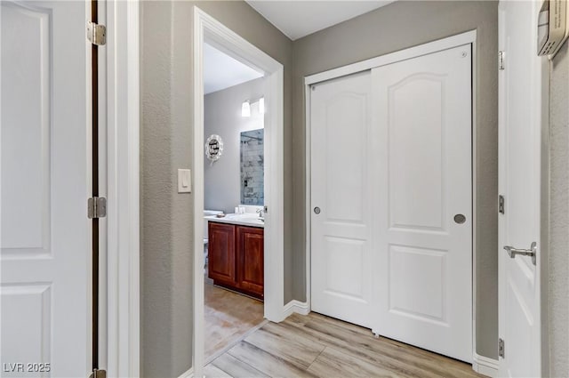 hallway with light wood-style floors, baseboards, and a sink