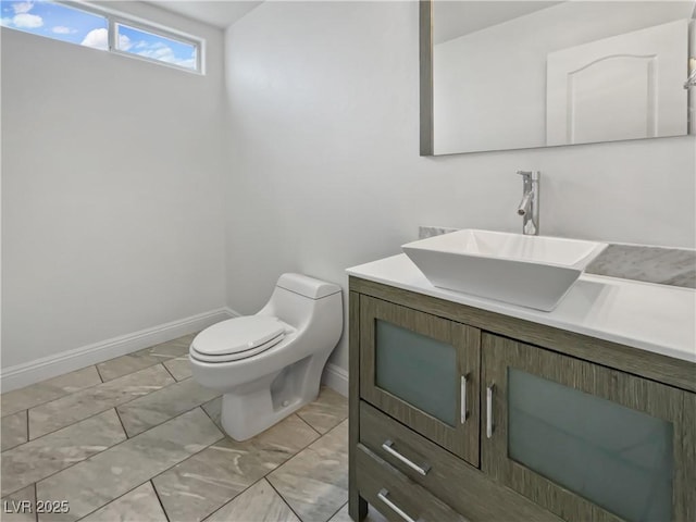 half bath with marble finish floor, toilet, vanity, and baseboards