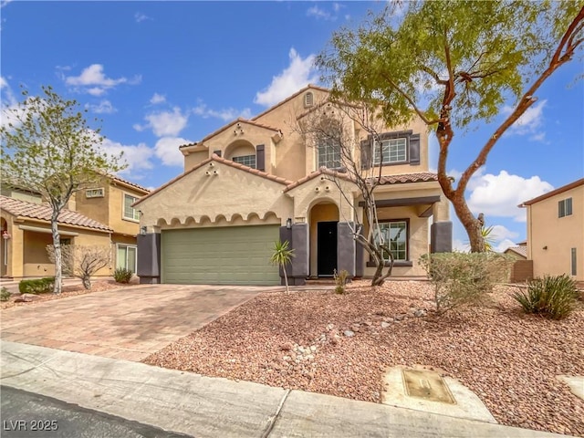 mediterranean / spanish house with a tiled roof, stucco siding, an attached garage, and decorative driveway