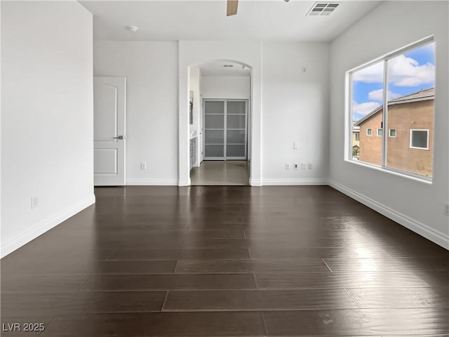 empty room with wood finished floors, arched walkways, visible vents, and baseboards