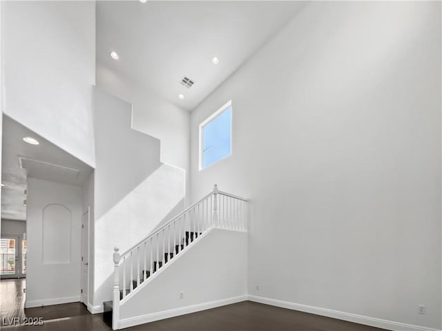 staircase with visible vents, wood finished floors, recessed lighting, baseboards, and a towering ceiling