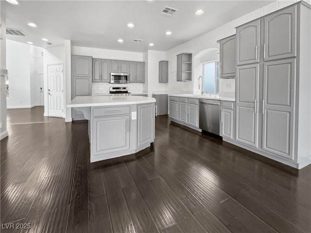 kitchen featuring visible vents, gray cabinets, open shelves, a kitchen island, and appliances with stainless steel finishes