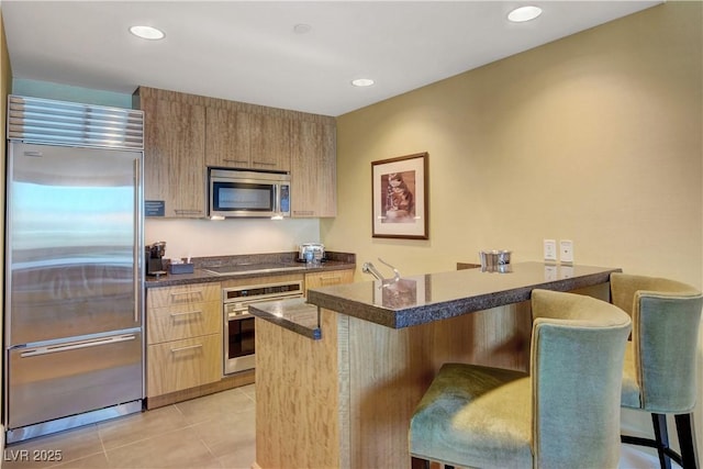 kitchen featuring light tile patterned floors, a kitchen breakfast bar, appliances with stainless steel finishes, dark countertops, and modern cabinets