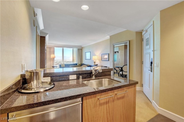 kitchen with baseboards, dark stone counters, open floor plan, a sink, and stainless steel dishwasher