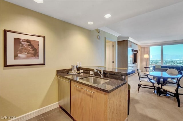 kitchen featuring baseboards, dark stone counters, dishwasher, a peninsula, and a sink