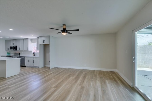 unfurnished living room featuring baseboards, light wood-type flooring, a wealth of natural light, and a sink