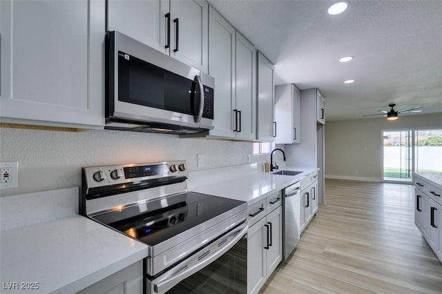 kitchen with baseboards, light wood finished floors, recessed lighting, a sink, and stainless steel appliances