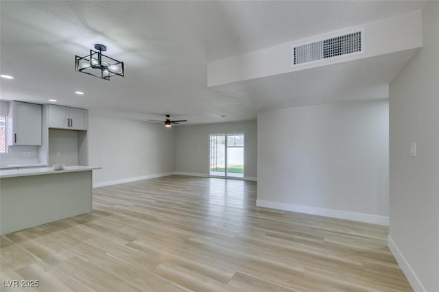 unfurnished living room with visible vents, light wood-style flooring, a ceiling fan, and baseboards